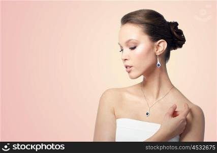 beauty, jewelry, wedding accessories, people and luxury concept - beautiful asian woman or bride with earring and pendant over beige background