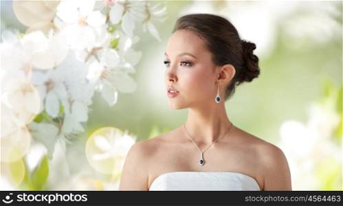 beauty, jewelry, wedding accessories, people and luxury concept - beautiful asian woman or bride with earring and pendant over natural spring cherry blossom background