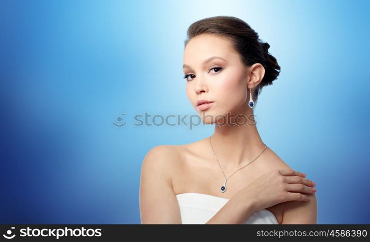 beauty, jewelry, wedding accessories, people and luxury concept - beautiful asian woman or bride with earring and pendant over blue background