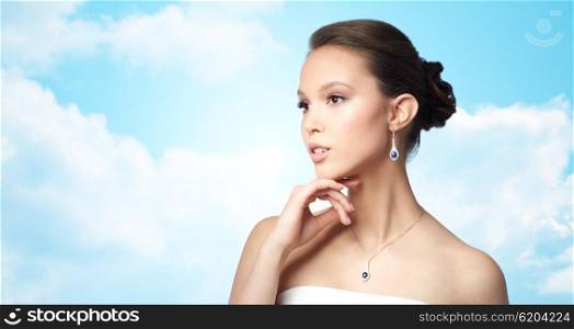 beauty, jewelry, wedding accessories, people and luxury concept - beautiful asian woman or bride with earring and pendant over blue sky and clouds background