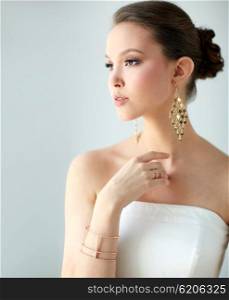 beauty, jewelry, wedding accessories, people and luxury concept - beautiful asian woman in white dress or bride with golden earrings and bracelet