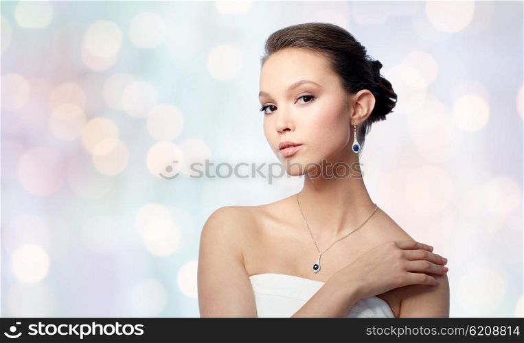 beauty, jewelry, wedding accessories, people and luxury concept - beautiful asian woman or bride with earring and pendant over blue holidays lights background