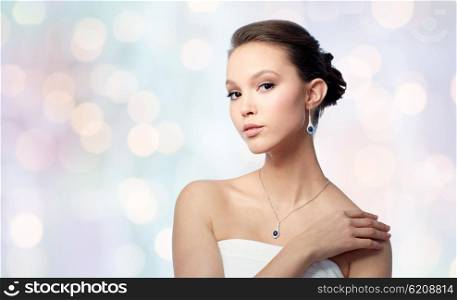 beauty, jewelry, wedding accessories, people and luxury concept - beautiful asian woman or bride with earring and pendant over blue holidays lights background