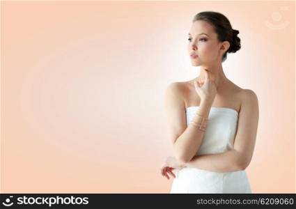 beauty, jewelry, wedding accessories, people and luxury concept - beautiful asian woman in white dress or bride with golden bracelet over beige background