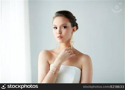 beauty, jewelry, wedding accessories, people and luxury concept - beautiful asian woman in white dress or bride with golden earrings and bracelet