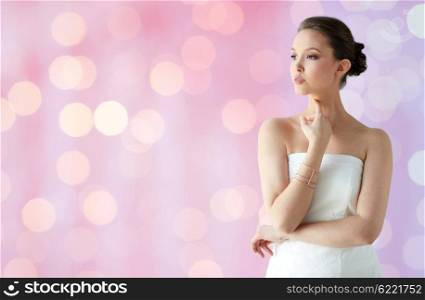 beauty, jewelry, wedding accessories, people and luxury concept - beautiful asian woman in white dress or bride with golden bracelet over holidays lights background