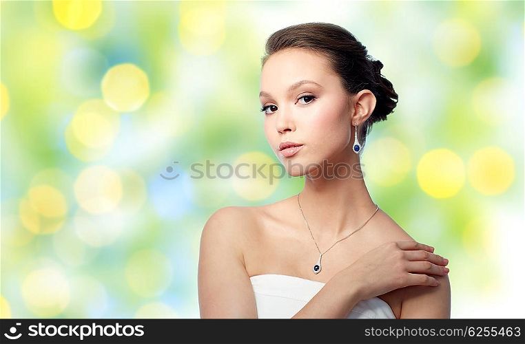 beauty, jewelry, wedding accessories, people and luxury concept - beautiful asian woman or bride with earring and pendant over summer green lights background