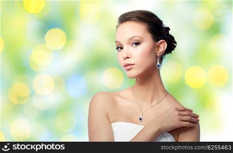 beauty, jewelry, wedding accessories, people and luxury concept - beautiful asian woman or bride with earring and pendant over summer green lights background