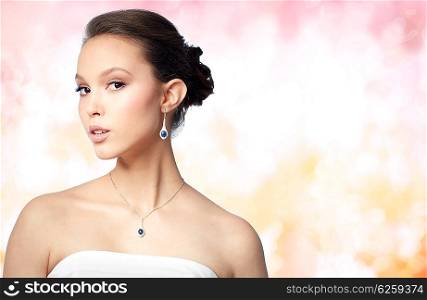 beauty, jewelry, wedding accessories, people and luxury concept - beautiful asian woman or bride with earring and pendant over holidays lights background