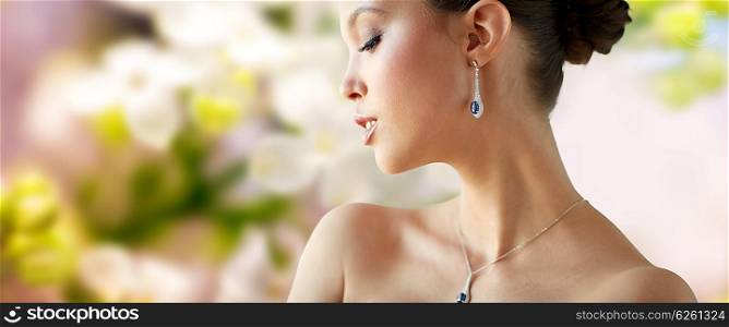 beauty, jewelry, wedding accessories, people and luxury concept - beautiful asian woman or bride with earring and pendant over natural spring lilac blossom background