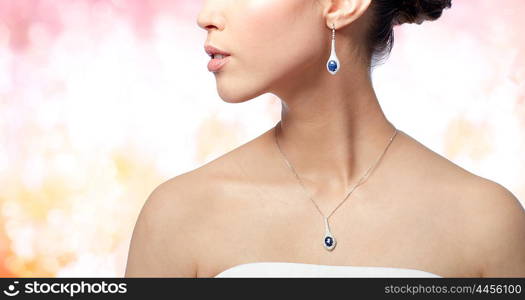 beauty, jewelry, wedding accessories, people and luxury concept - close up of beautiful asian woman or bride with earring and pendant over holidays lights background