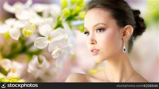 beauty, jewelry, wedding accessories, people and luxury concept - close up of beautiful asian woman or bride with earring over natural spring lilac blossom background