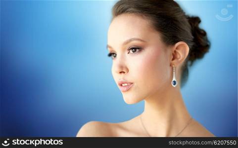 beauty, jewelry, wedding accessories, people and luxury concept - close up of beautiful asian woman or bride with earring over blue background