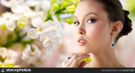 beauty, jewelry, wedding accessories, people and luxury concept - close up of beautiful asian woman or bride with earring and finger ring over natural spring lilac blossom background