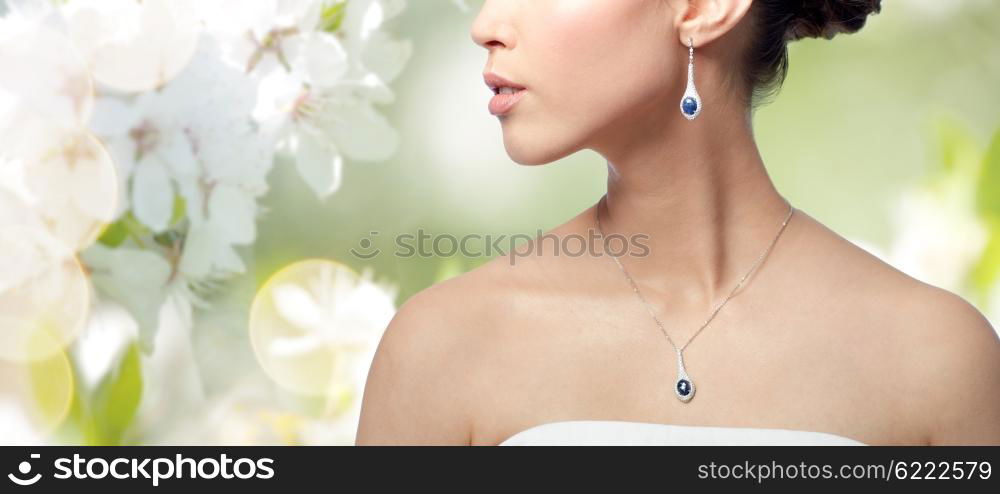 beauty, jewelry, wedding accessories, people and luxury concept - close up of beautiful asian woman or bride with earring and pendant over natural spring cherry blossom background