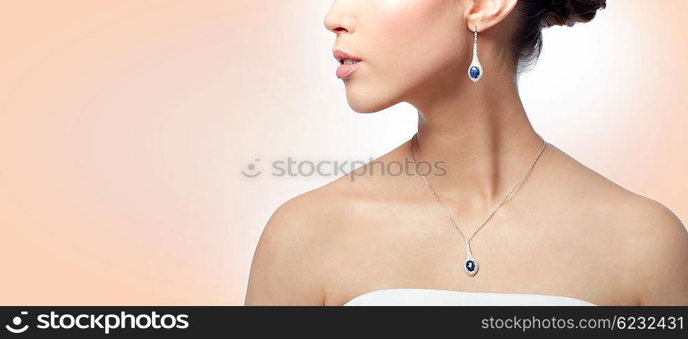 beauty, jewelry, wedding accessories, people and luxury concept - close up of beautiful asian woman or bride with earring and pendant over beige background