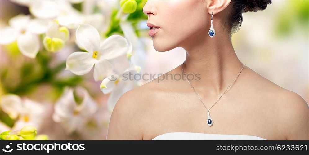beauty, jewelry, wedding accessories, people and luxury concept - close up of beautiful asian woman or bride with earring and pendant over natural spring lilac blossom background