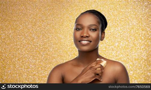 beauty, luxury and body care concept - portrait of happy smiling young african american woman with bare shoulders over golden glitter background. portrait of young african american woman