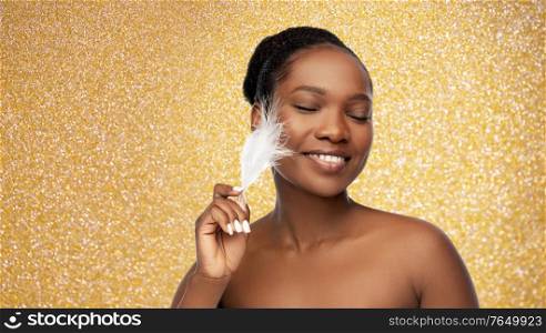 beauty, luxury and people concept - portrait of happy smiling young african american woman with bare shoulders and feather over golden glitter background. happy african american woman with feather