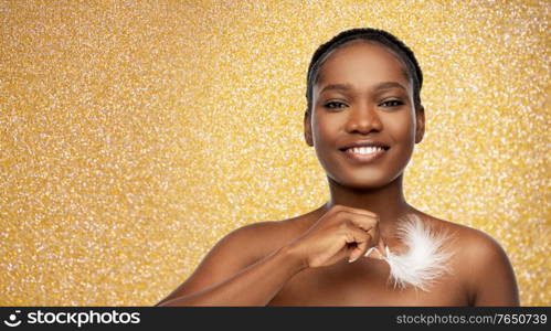 beauty, luxury and people concept - portrait of happy smiling young african american woman with bare shoulders and feather over golden glitter background. happy african american woman with feather