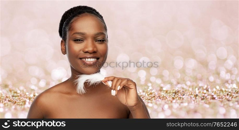 beauty, luxury and people concept - portrait of happy smiling young african american woman with bare shoulders and feather over beige glitter background. happy african american woman with feather