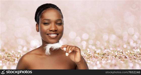 beauty, luxury and people concept - portrait of happy smiling young african american woman with bare shoulders and feather over beige glitter background. happy african american woman with feather