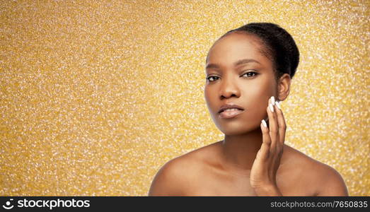 beauty, luxury and people concept - portrait of young african american woman with bare shoulders touching her face over golden glitter on background. portrait of african woman touching her face