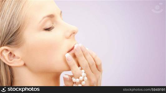 beauty, luxury, people, advertisement and jewelry concept - face of beautiful woman with sea pearls beads in hand over violet background