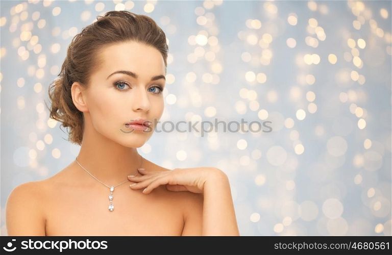 beauty, luxury, people, holidays and jewelry concept - beautiful woman wearing shiny diamond pendant over lights background