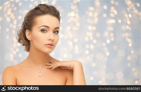 beauty, luxury, people, holidays and jewelry concept - beautiful woman wearing shiny diamond pendant over lights background