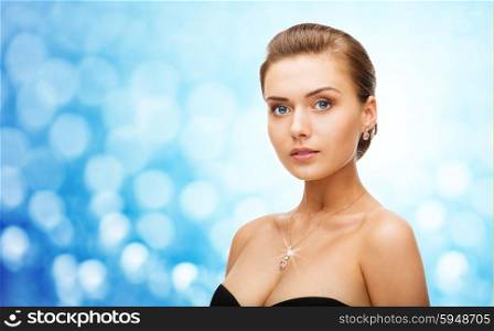 beauty, luxury, people, holidays and jewelry concept - beautiful woman wearing shiny diamond earrings and pendant over blue lights background