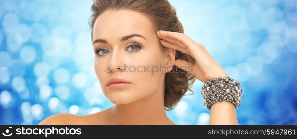 beauty, luxury, people, holidays and jewelry concept - beautiful woman with bracelets over blue background