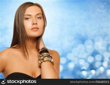 beauty, luxury, people, holidays and jewelry concept - beautiful woman with bracelets over blue background