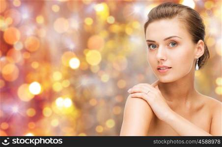 beauty, luxury, people, holidays and jewelry concept - beautiful woman with diamond ring and earrings over lights background