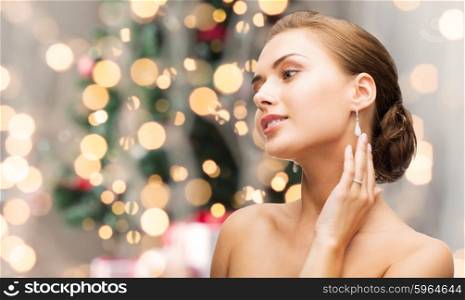 beauty, luxury, people, holidays and jewelry concept - beautiful woman with diamond earrings over christmas lights background