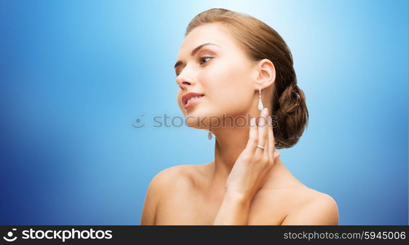 beauty, luxury, people, holidays and jewelry concept - beautiful woman with diamond earrings over blue background