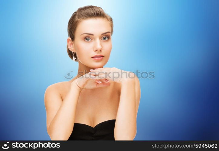 beauty, luxury, people, holidays and jewelry concept - beautiful woman with diamond earrings over blue background