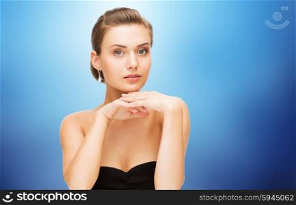 beauty, luxury, people, holidays and jewelry concept - beautiful woman with diamond earrings over blue background