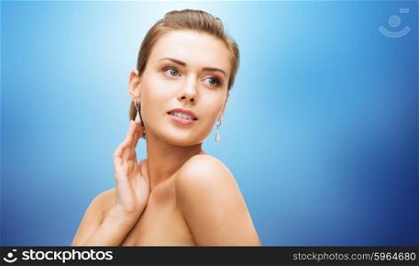 beauty, luxury, people, holidays and jewelry concept - beautiful woman with diamond earrings over blue background