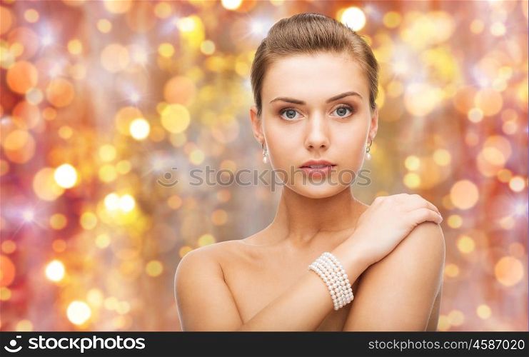 beauty, luxury, people, holidays and jewelry concept - beautiful woman with pearl earrings and bracelet over lights background
