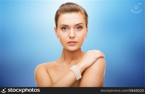 beauty, luxury, people, holidays and jewelry concept - beautiful woman with pearl earrings and bracelet over blue background