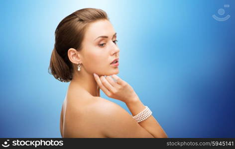 beauty, luxury, people, holidays and jewelry concept - beautiful woman with pearl earrings and bracelet over blue background