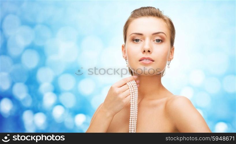 beauty, luxury, people, holidays and jewelry concept - beautiful woman with pearl earrings and bracelet over blue lights background