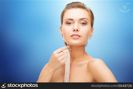 beauty, luxury, people, holidays and jewelry concept - beautiful woman with pearl earrings and bracelet over blue lights background