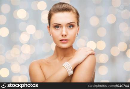 beauty, luxury, people, holidays and jewelry concept - beautiful woman with pearl earrings and bracelet over lights background