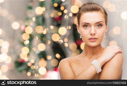 beauty, luxury, people, holidays and jewelry concept - beautiful woman with pearl earrings and bracelet over christmas lights background