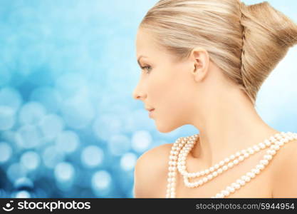 beauty, luxury, people, holidays and jewelry concept - beautiful woman with sea pearl necklace or beads over blue lights background