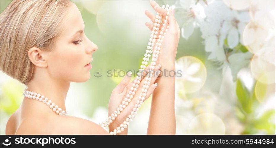 beauty, luxury, people, holidays and jewelry concept - beautiful woman with sea pearl necklace or beads over cherry blossom background