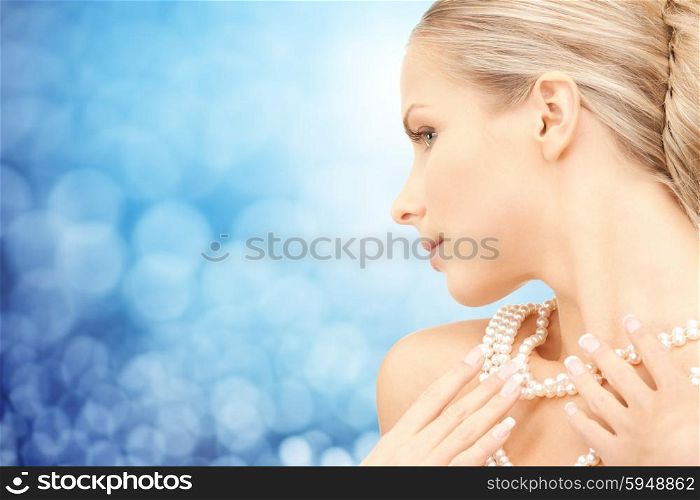 beauty, luxury, people, holidays and jewelry concept - beautiful woman with sea pearl necklace or beads over blue lights background