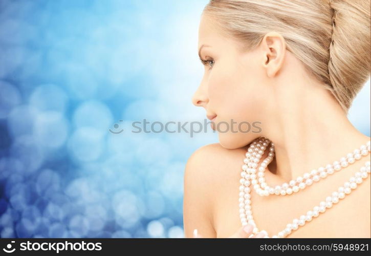 beauty, luxury, people, holidays and jewelry concept - beautiful woman with sea pearl necklace or beads over blue lights background